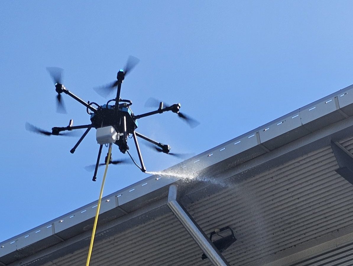 Revolutionizing Exterior Cleaning with Drone Technology: Safe & Efficient Building Maintenance Drone performing high-pressure exterior cleaning on a commercial building roof, showcasing advanced cleaning technology.